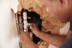 Over shoulder view of middle aged man repairing burst pipe