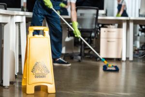 cleaner washing floor with mop near wet floor caution sign