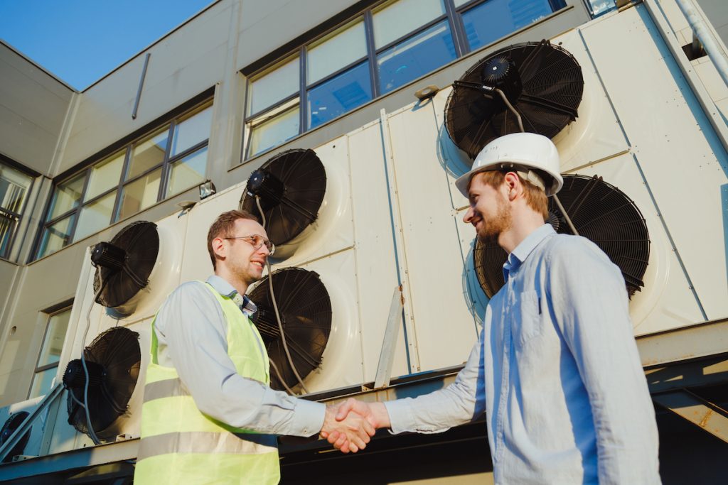 owner and manager next to AC units agreeing to make the industry standard hvac business profit margin