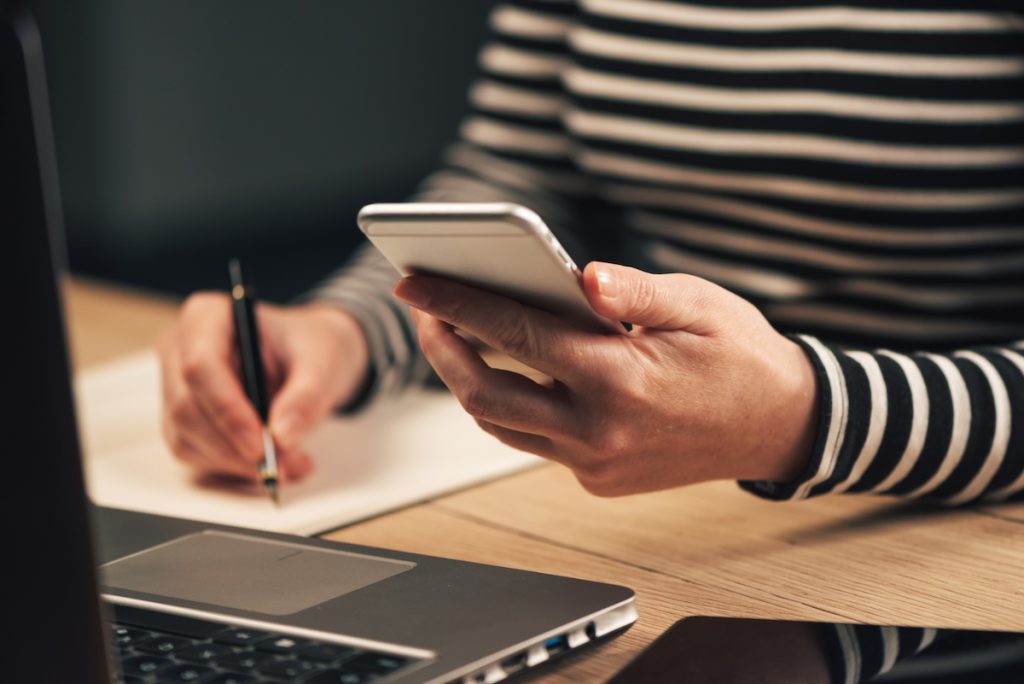 woman holding phone and computer and writing field service metrics on paper